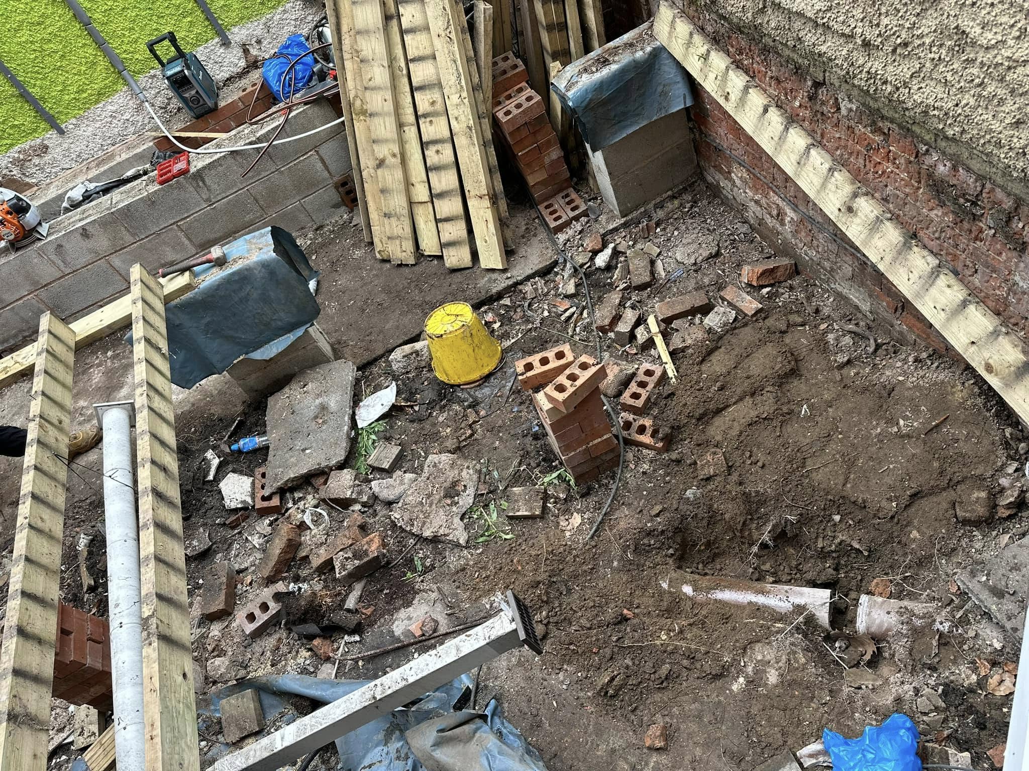 An excavated area with visible drainage pipes, soil, and building materials during a repair or installation project.