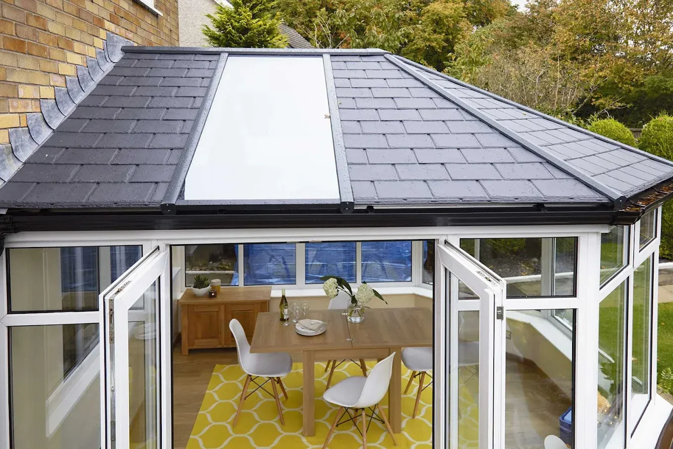 A modern conservatory with a new tiled and glazed warm roof, white UPVC windows, and open French doors leading into a bright dining space.