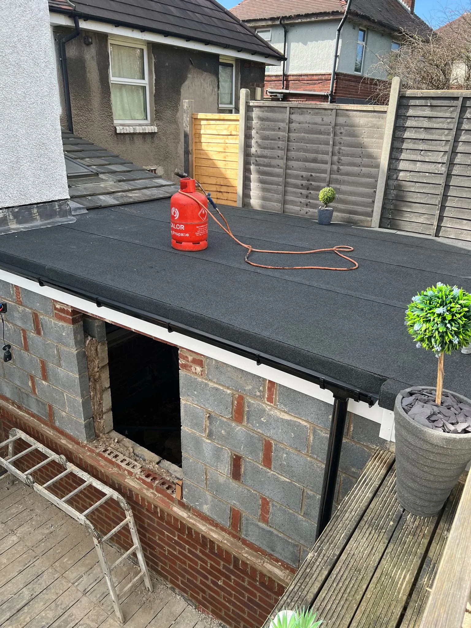 Newly installed flat roof on a residential extension with guttering and gas bottle