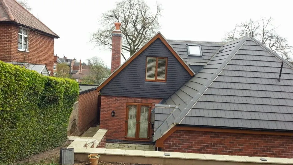 New grey tiled roof with dormer and Velux window on a brick extension