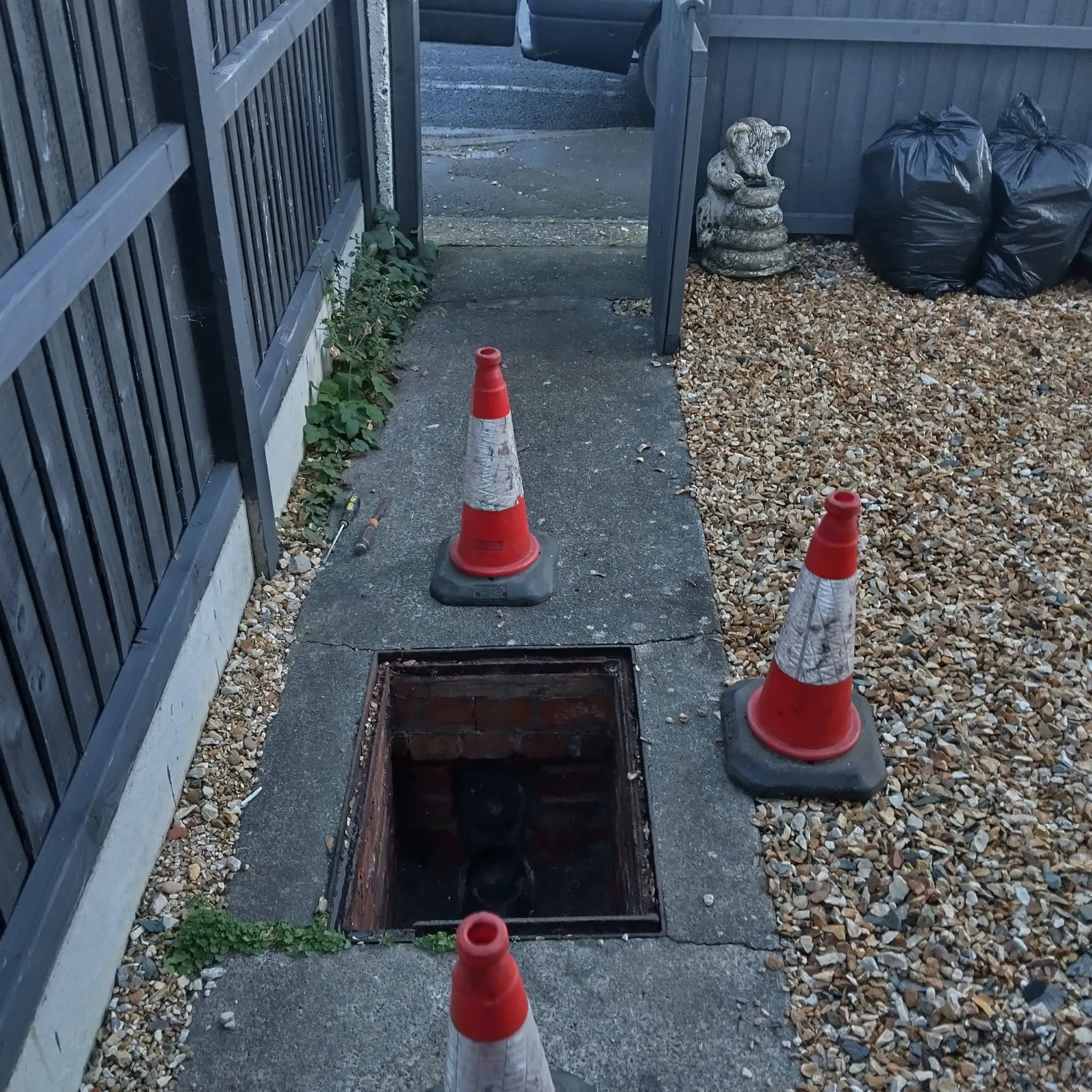 An open drain cover marked with traffic cones