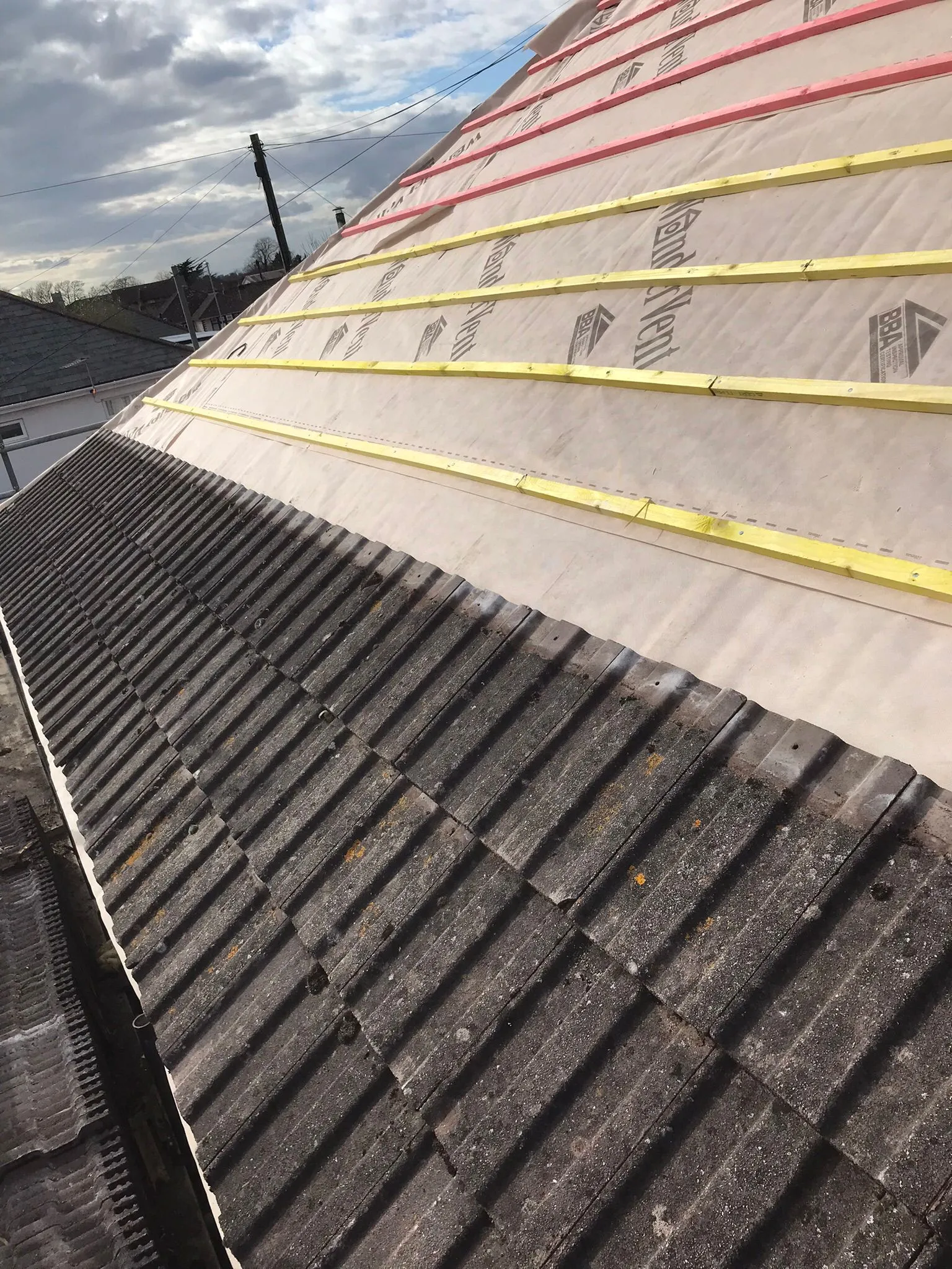 Pitched roof in Southampton showing old, moss-covered tiles alongside new roofing underlayment and timber battens during a repair or re-tiling project.