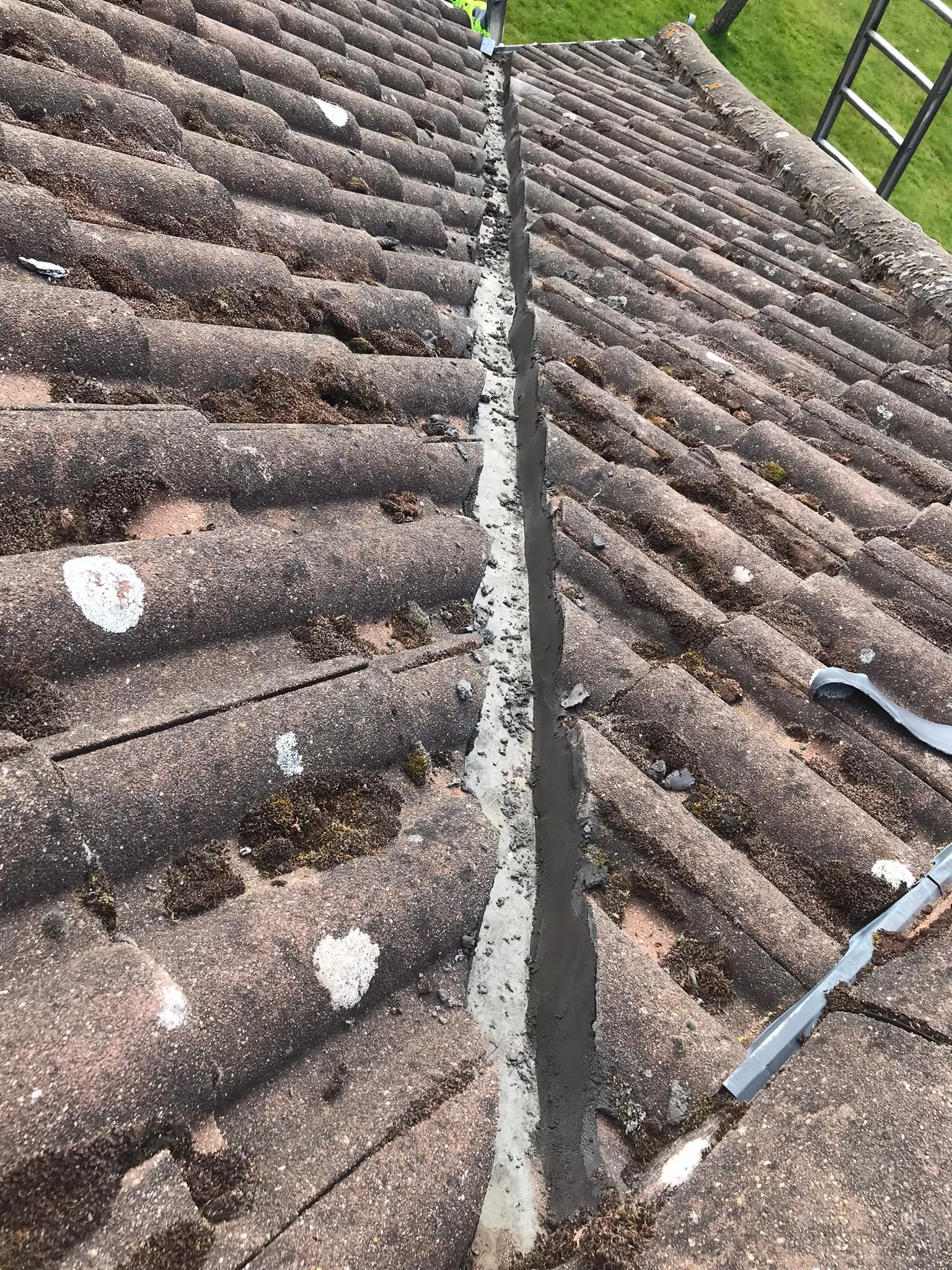 Tiled roof valley showing fresh mortar between sections of old, moss-covered roof tiles.