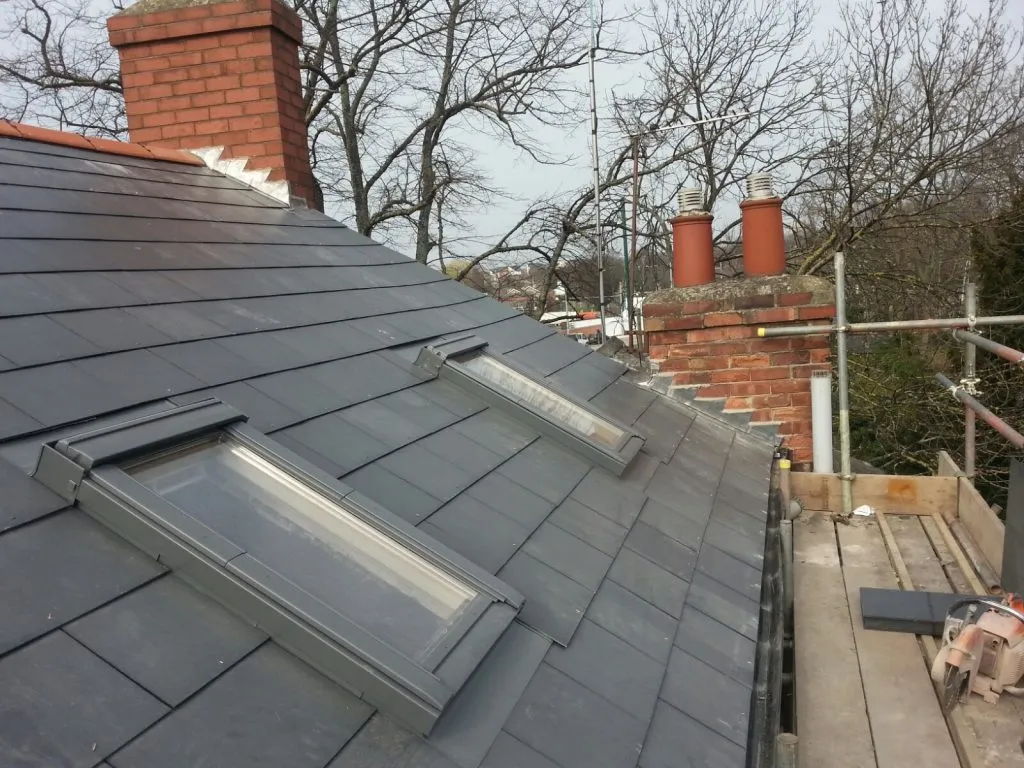 Newly installed grey tiled pitched roof with two Velux windows and a brick chimney stack.