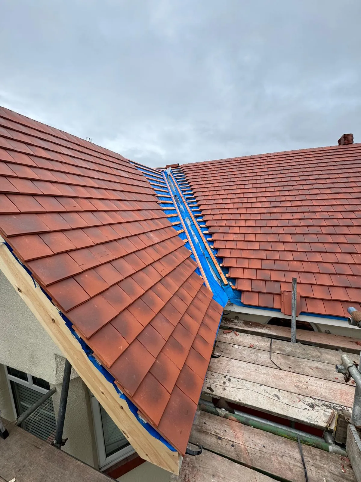 New red roof tiles being installed on a house, with the roof partially tiled and underlayment exposed.