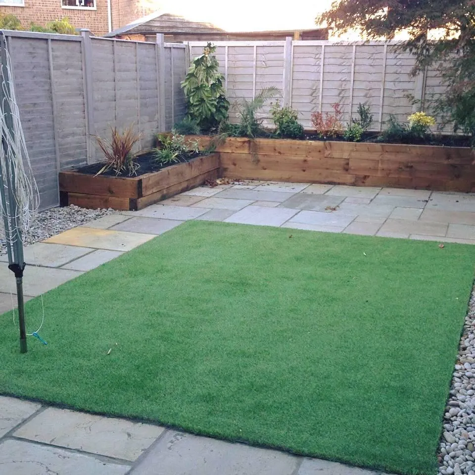 Artificial grass lawn and paved patio in a landscaped garden with raised wooden planters.