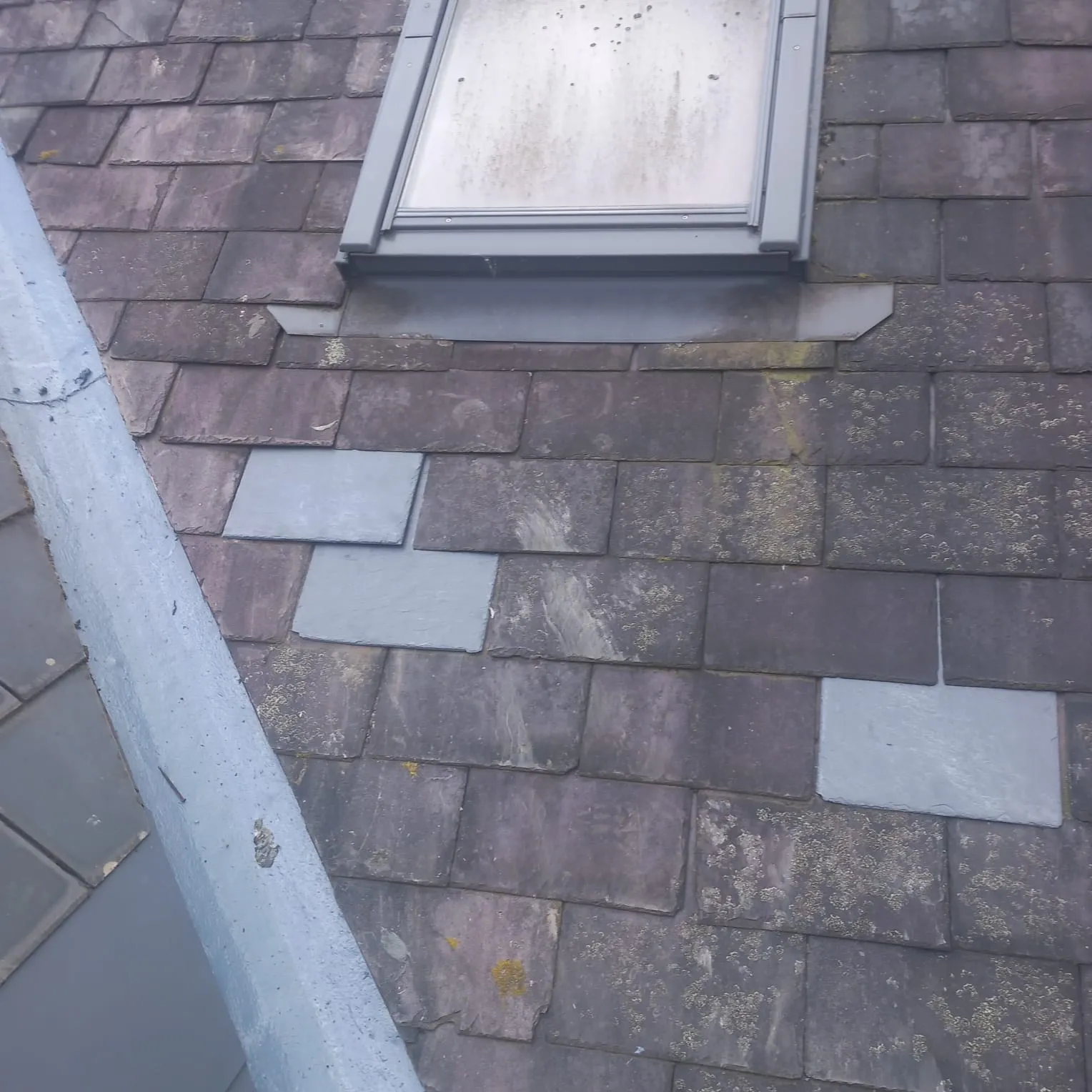 Slate roof with skylight, showing old and new tiles, moss, and lead valley. Illustrates common needs for roof repair and maintenance in Leicester.