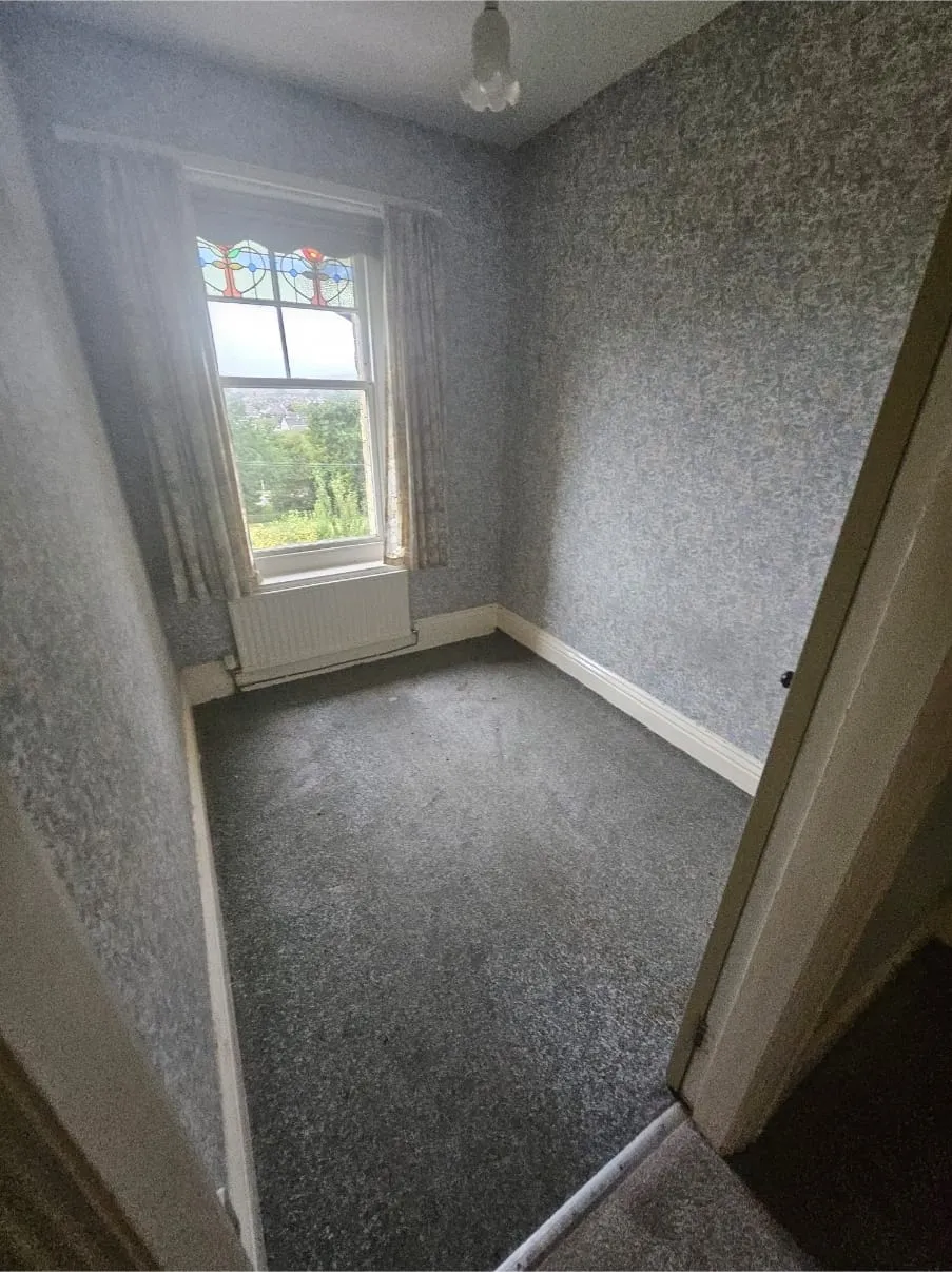 A clean, empty room with grey carpet and patterned wallpaper after a house clearance, ready for new occupants.