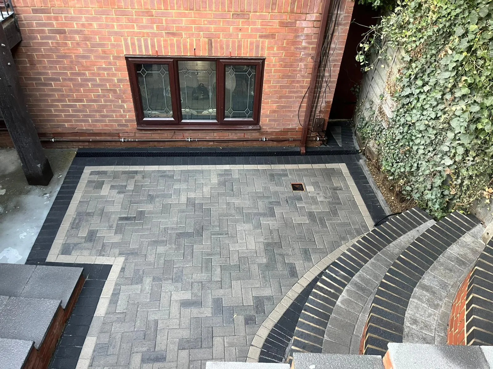 Newly installed block paving patio in herringbone pattern with integrated drainage and curved steps leading down.