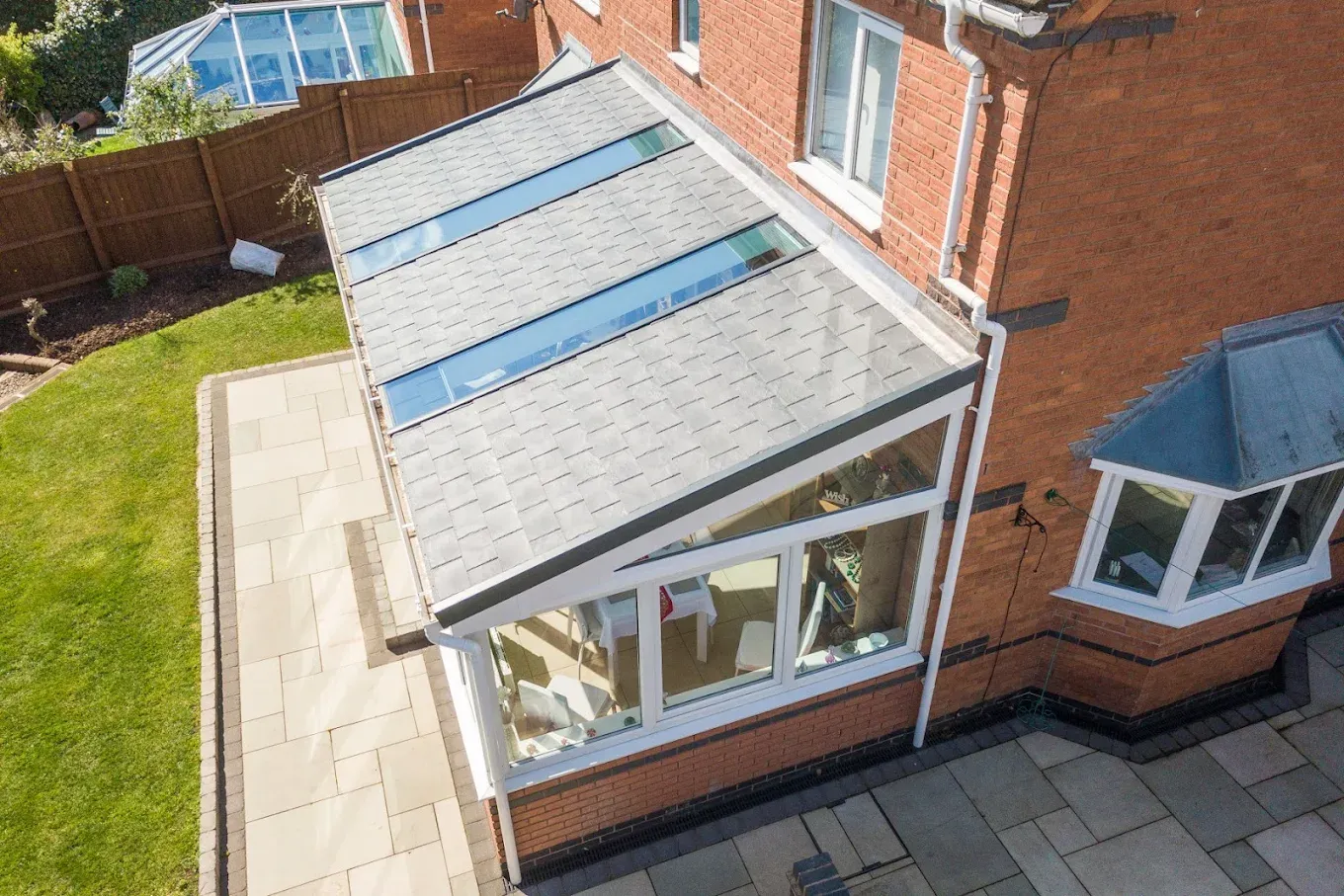 Newly fitted grey tiled conservatory roof with skylights on a house extension, showing the patio and garden.