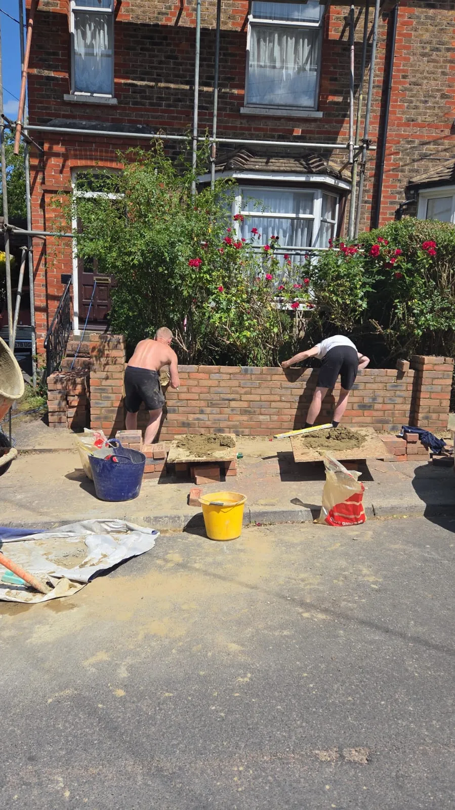 Two builders constructing a brick wall at the front of a house in Haywards Heath.