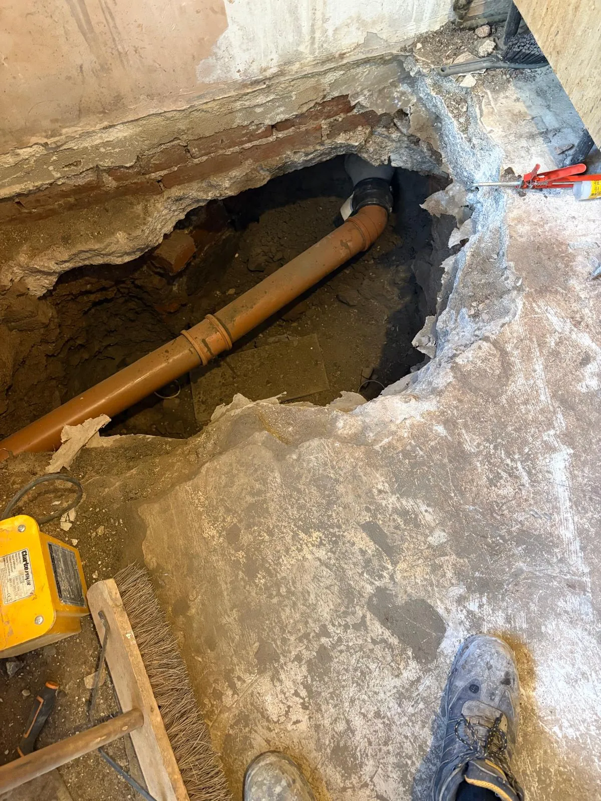 Excavated floor exposing a brown foul water drainage pipe during installation or repair.