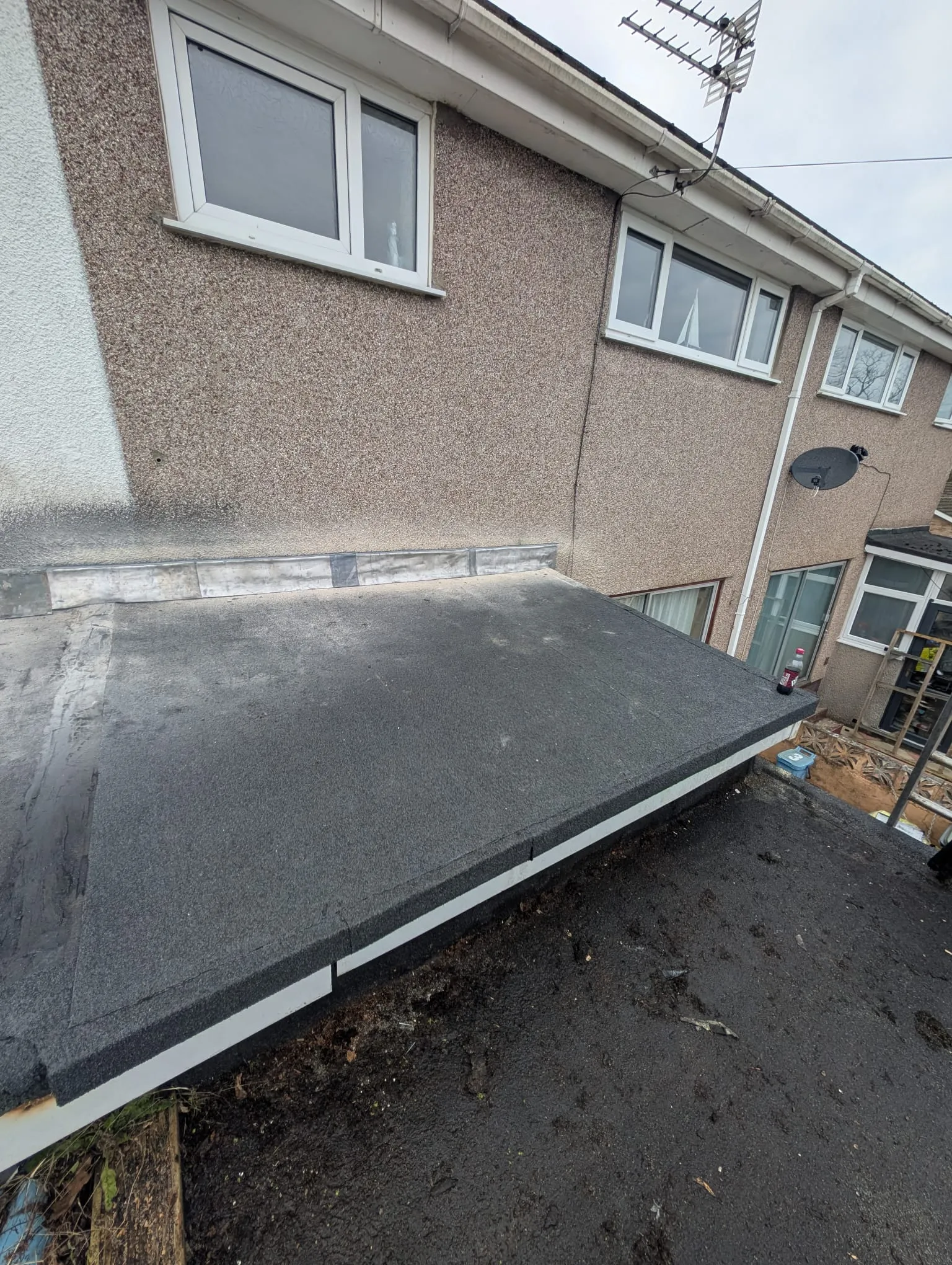 A close-up view of a recently installed or repaired flat felt roof on a residential building.