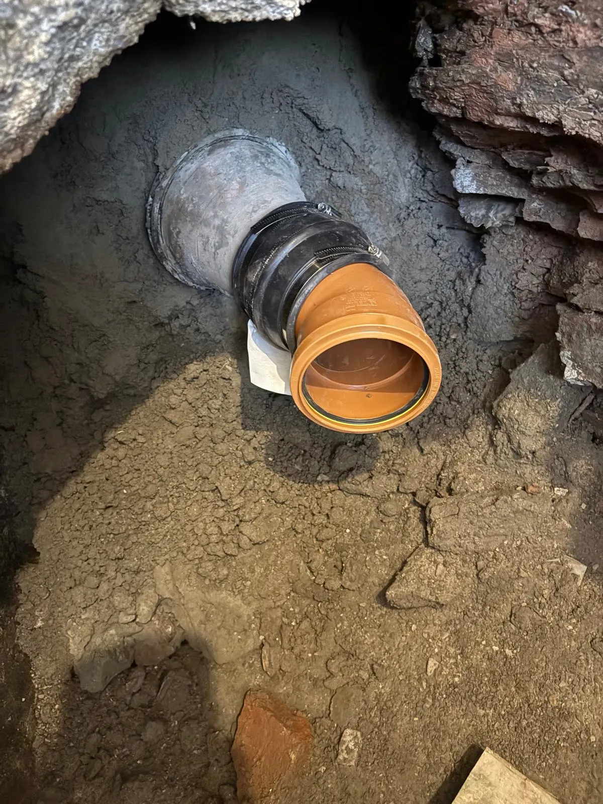 An orange drainage pipe connected to a grey pipe in the ground, showing a new installation or repair work.