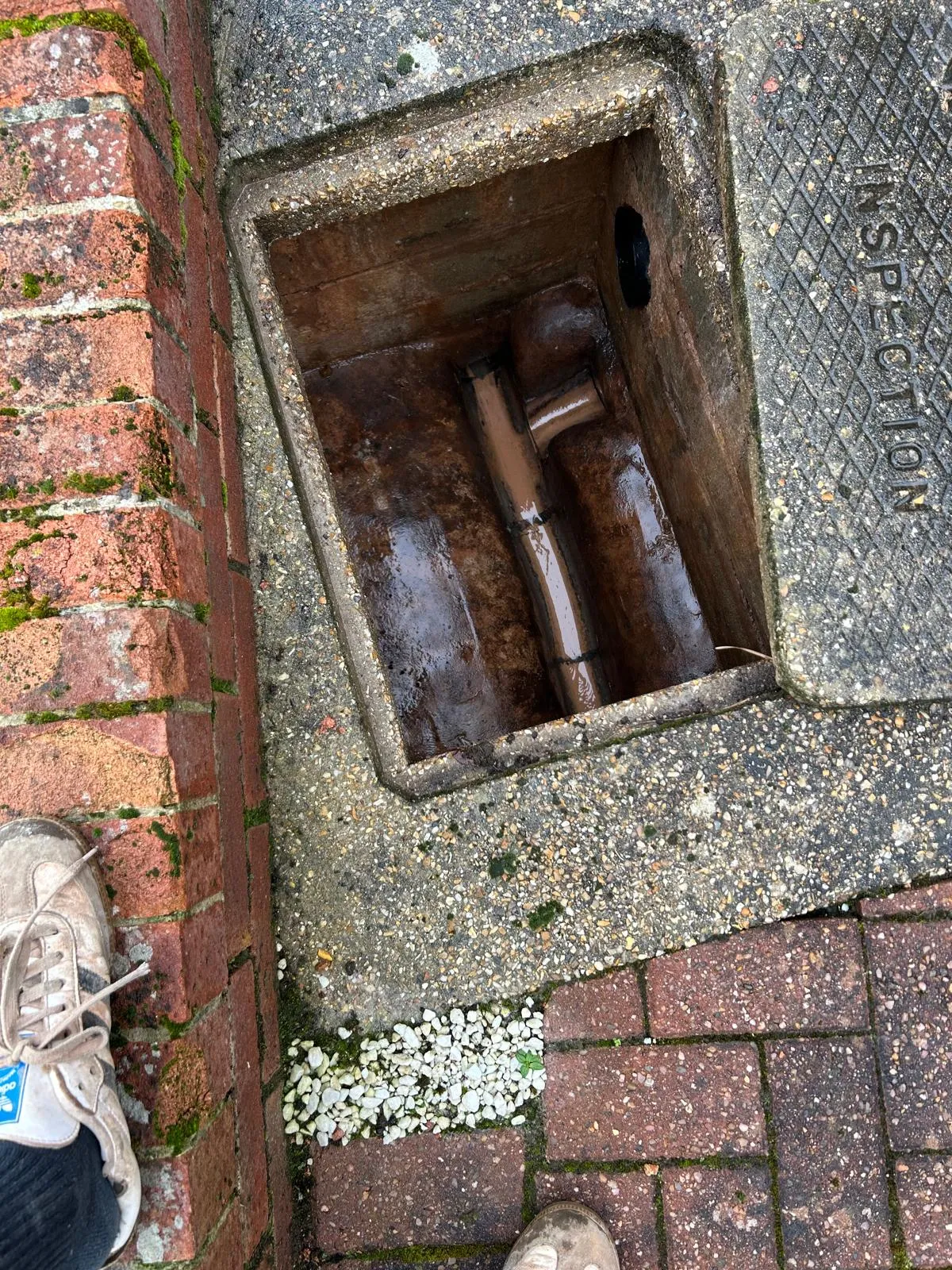 An open manhole or inspection chamber showing a blocked drain with dirty water and pipework.