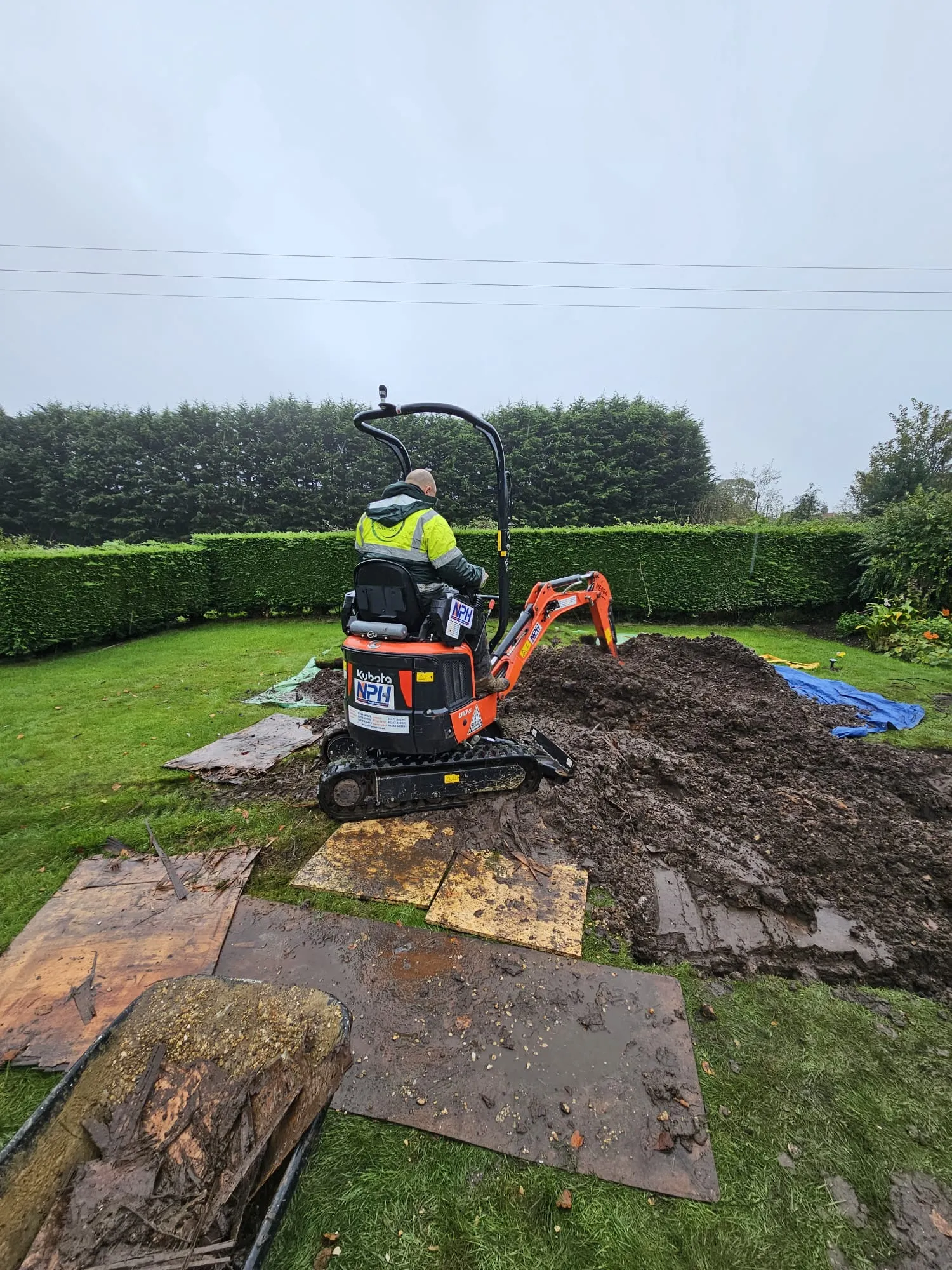 Mini excavator digging a trench in a garden for drainage or groundwork services