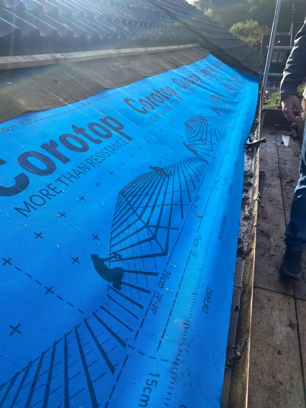Blue roofing underlayment being installed on a pitched roof