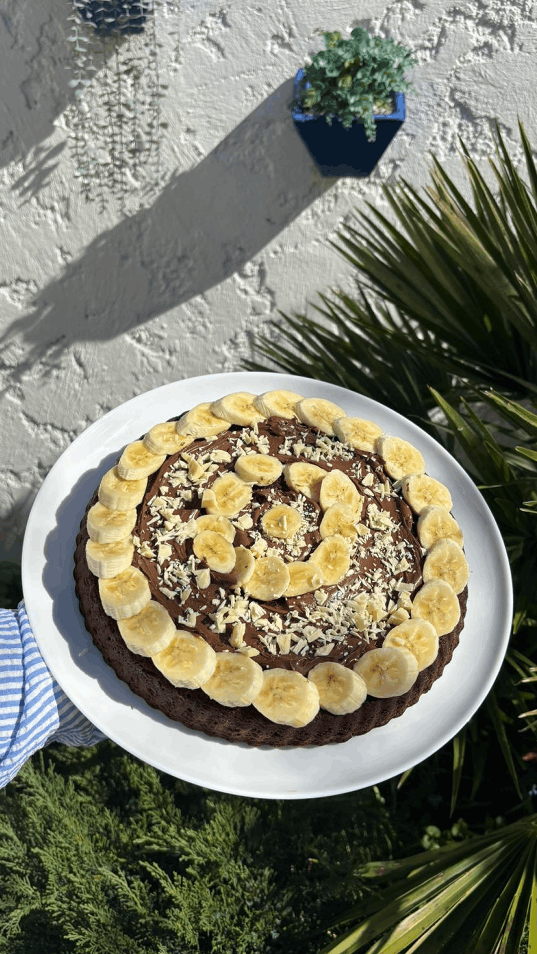 Une base de gâteau au chocolat intense et moelleuse, surmontée d'une onctueuse ganache au chocolat noir. Ce gâteau est généreusement garni de rondelles de bananes fraîches disposées en rosace, apportant une douceur naturelle qui équilibre la force du cacao. Quelques copeaux de chocolat blanc viennent saupoudrer l'ensemble pour une note lactée et croquante.