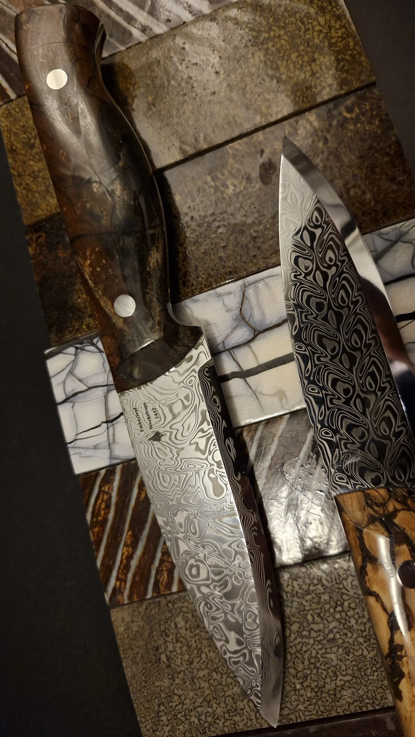 Knife 2417 beside a second, contrasting damascus blade on the tile bench