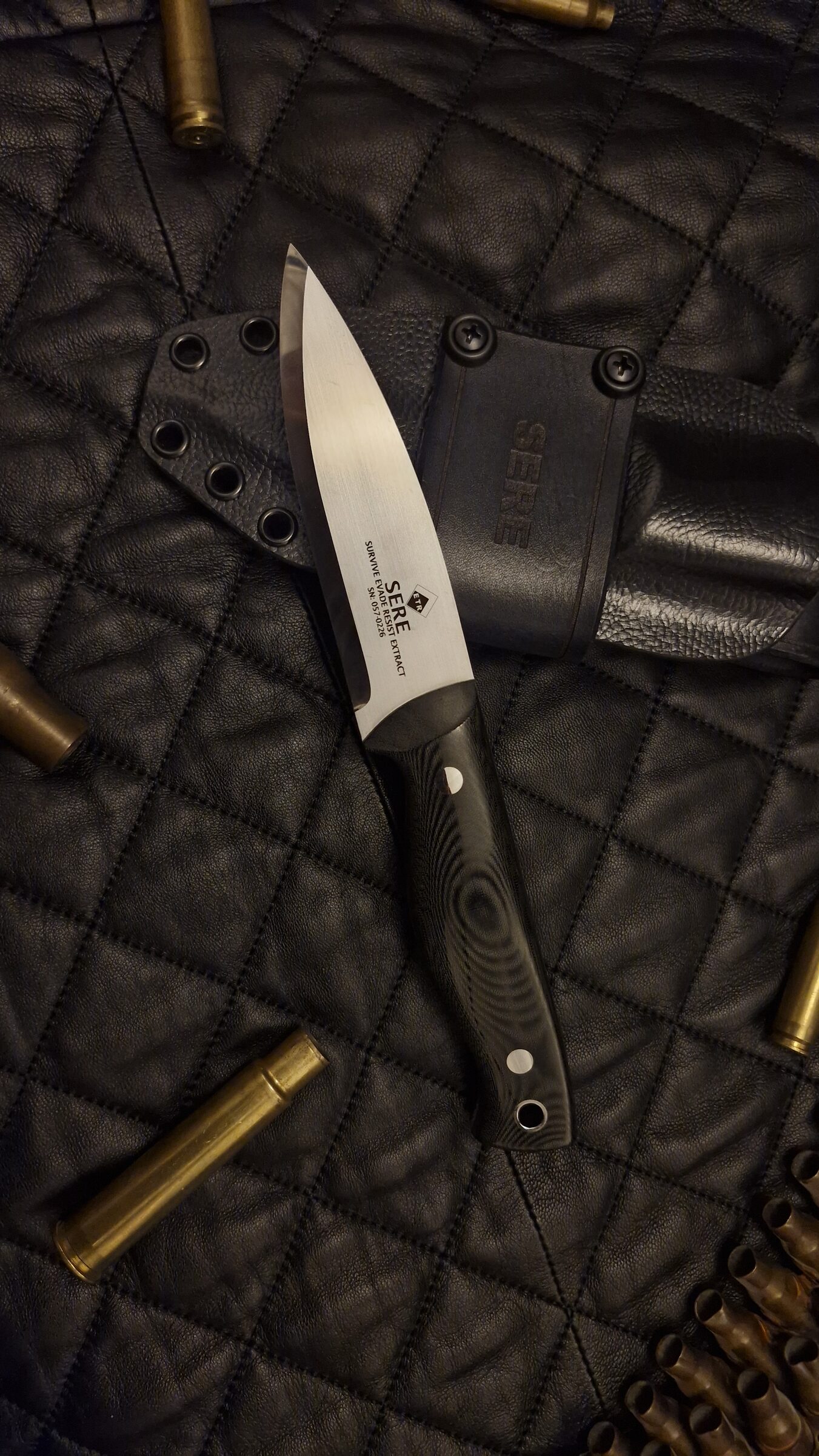 SERE knife in full side profile, serial number etched on the blade, sheath behind