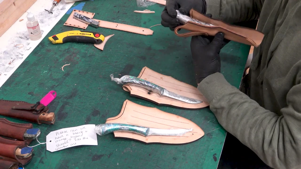 Two damascus daggers being sized to their leather sheath patterns on the green workbench