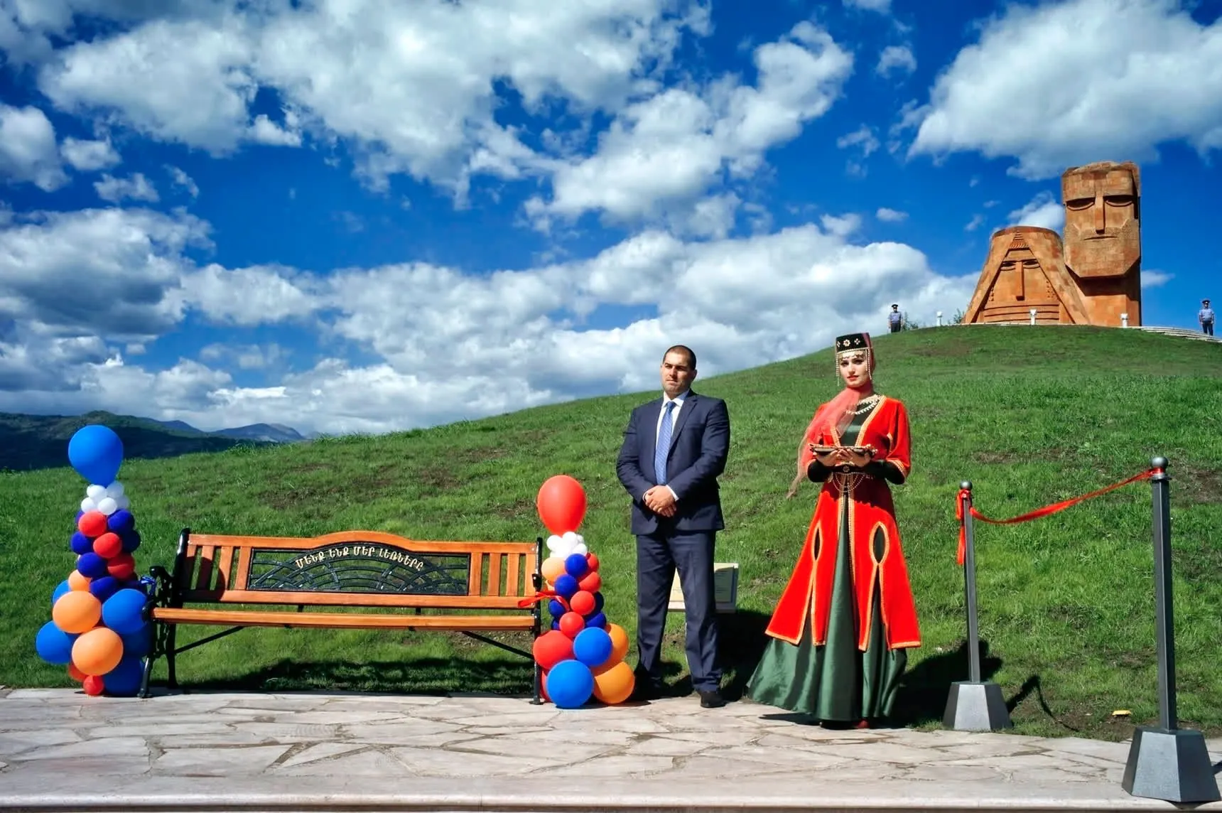 Deux personnes se tiennent devant un monument, à côté d'un banc décoré de ballons.