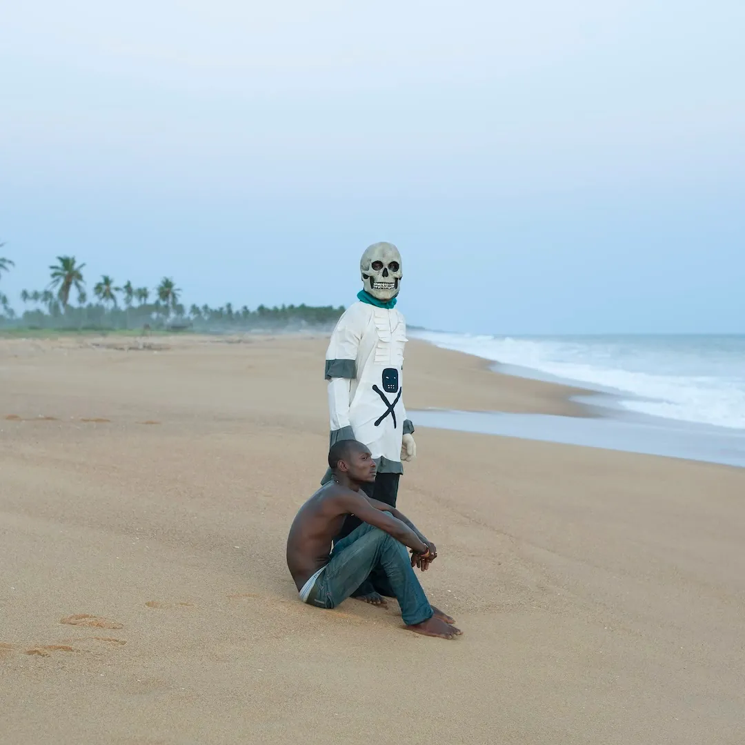 Deux hommes sur la plage dont un avec un masque de tête squelette. 