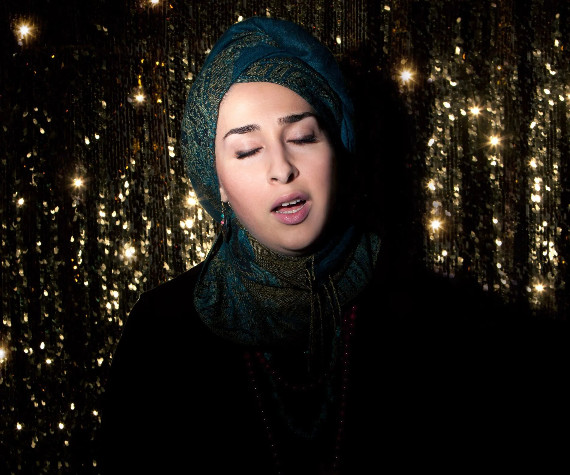 Une femme iranienne chante devant un rideau pailleté. 
