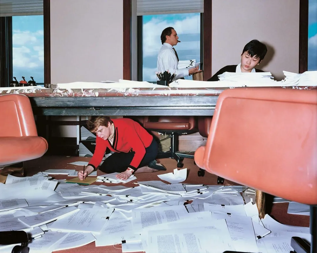 Un bureau avec des feuilles de partout et un homme sous la table. 