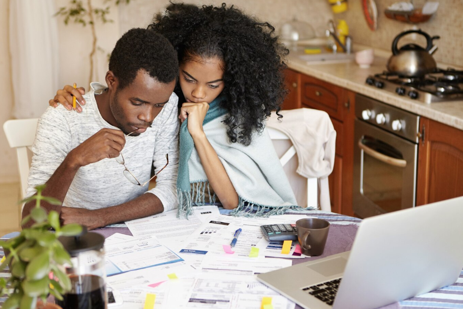 Parents are discussing educational expenses with tools like a laptop, calculator, and charts on the table.